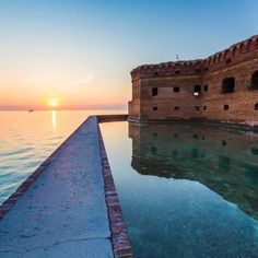 the sun is setting behind an old brick wall by the water's edge,