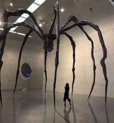 a giant spider sculpture is in the middle of a room with people walking around it