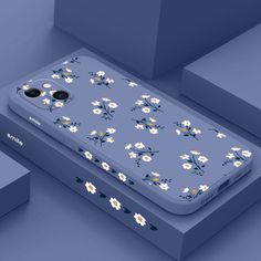 an iphone case with daisies and black buttons sits on a blue surface next to boxes