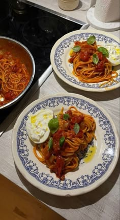 two plates of spaghetti with sauce and eggs on the side, next to a stove