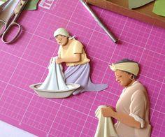 paper cutouts of two women sitting on a cutting board with scissors and other crafting supplies