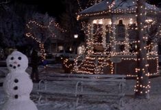 a snowman is standing in front of a gazebo with lights all around it