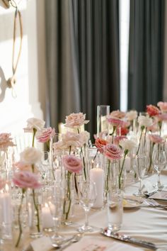 the table is set with candles and pink flowers in vases on top of each other