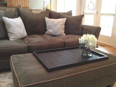 a living room with a brown couch and white flowers on the coffee table in front of it