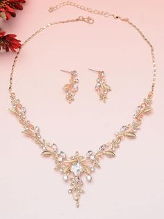 a necklace and earring set on a pink surface with flowers in the back ground