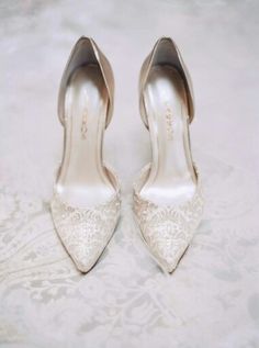 a pair of white high heel shoes sitting on top of a lace covered table cloth