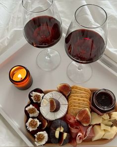 two glasses of red wine and cheese on a tray with crackers, figs, and grapes