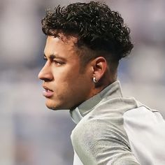 a close up of a man with curly hair wearing a gray shirt and earrings