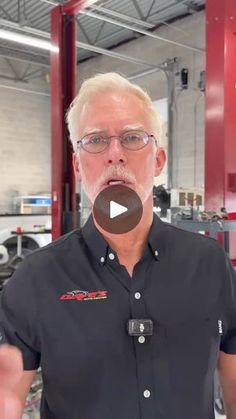 an older man wearing glasses and a black shirt is talking to the camera in a garage