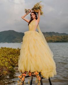 a woman in a yellow dress is standing on a stool near the water with flowers