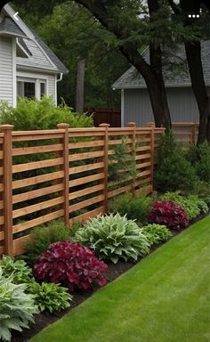 a wooden fence in front of a house surrounded by plants and flowers on the grass