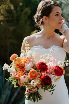 a woman in a white dress holding a bouquet of red and orange flowers on her wedding day