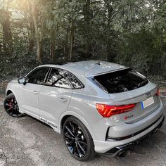 the rear end of a silver car parked in front of some trees