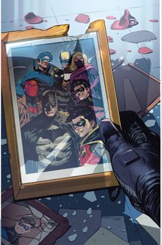 a person holding up a framed photo with batmans on it and other comic characters in the background