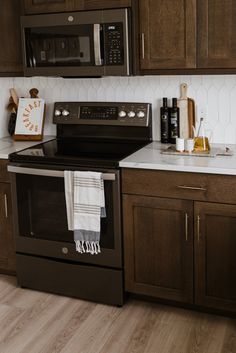 a kitchen with brown cabinets and white counter tops, black appliances and wooden flooring