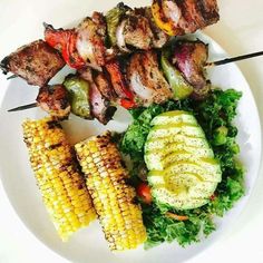 a white plate topped with meat and veggies next to corn on the cob