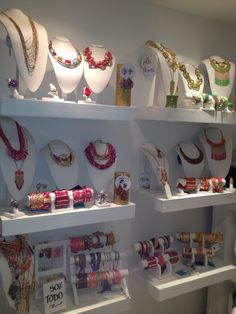 many necklaces and bracelets are on display in a store window with white shelves