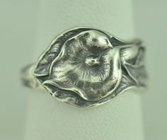 a silver ring with a flower design on the front and center, sitting on a white surface