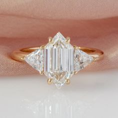 a three stone diamond ring on top of a pink satin baguette with gold accents