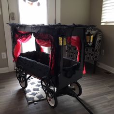 a black cart with red curtains on it in the middle of a floored room