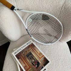 a tennis racket sitting on top of a white chair next to a magazine cover