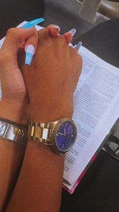 a woman's hand with a watch and pen on her wrist next to an open book