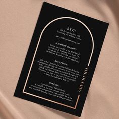 a black and gold wedding card with an arch in the middle on a satin background