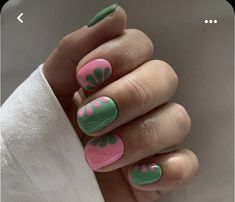 a woman's hand with green and pink nail polish on her nails, while she is wearing a white shirt