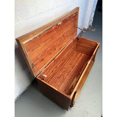 an open wooden box sitting on the ground next to a white wall and cement floor