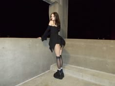 a woman in black dress leaning against concrete wall