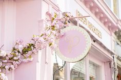 a pink storefront with a sign that says p on the front and flowers hanging from it