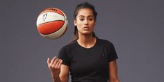 a woman holding a basketball in her hand and looking at the ball above her head