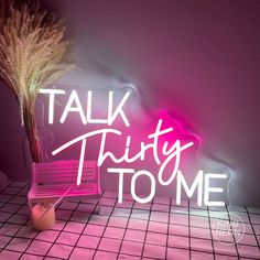 a neon sign that says talk thirty to me next to a pink chair with a plant in it