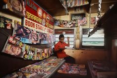 a man sitting in front of a store filled with magazines