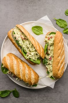 two sandwiches are sitting on a plate with green leafy leaves around them and one is cut in half