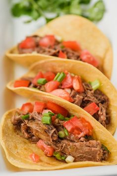 three tacos filled with meat, tomatoes and green onions on a white platter