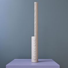 a tall white sculpture sitting on top of a purple table next to a gray wall