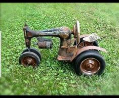 an old rusty toy tractor sitting in the grass with two forks on it's wheels