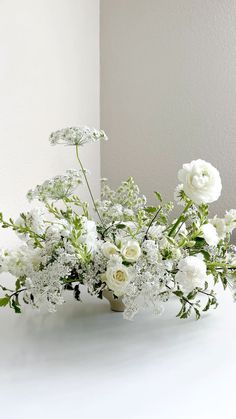 a vase filled with white flowers sitting on top of a table next to a wall