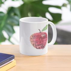 a white coffee mug sitting on top of a wooden table next to a book and plant