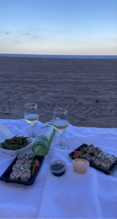 two glasses of wine are sitting on a table with sushi and other food at the beach