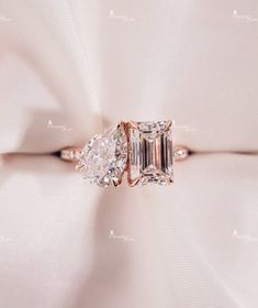 an engagement ring with two pear shaped diamonds on top of a white satin material background