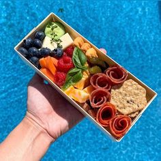 a hand holding a box of fruit and crackers next to a blue swimming pool