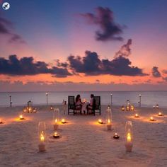 two people sitting at a table with candles on the beach