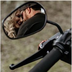 a man and woman are hugging in front of a motorcycle mirror