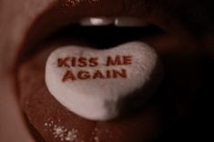 the word kiss me again written on a white heart shaped lollipop in someone's mouth