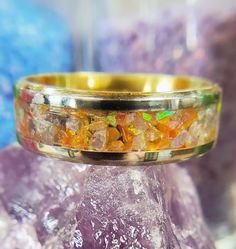 a gold ring with colorful stones on it sitting on top of some rocks and purple crystals