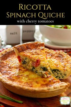 a quiche with cherry tomatoes and spinach is shown on a wooden platter