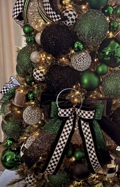 a christmas tree decorated with green and black balls, ornaments and bows is shown in this image