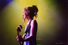 a woman standing in front of a green light holding a guitar and looking at the camera